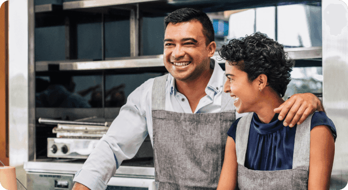 A man and woman standing side by side wearing aprons.